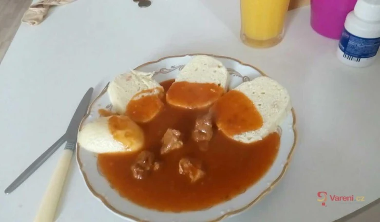 Připravený vepřový guláš s chlebovými rohlíky na talíři.