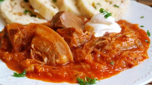 Perkelt s červenou kapustou a chlebem na talíři.