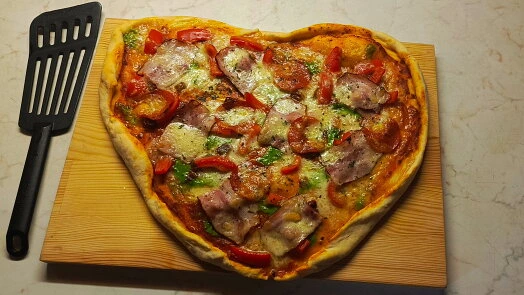 Srdcovitá nezkvašená pizzu s uzeným masem na dřevěném prknu.