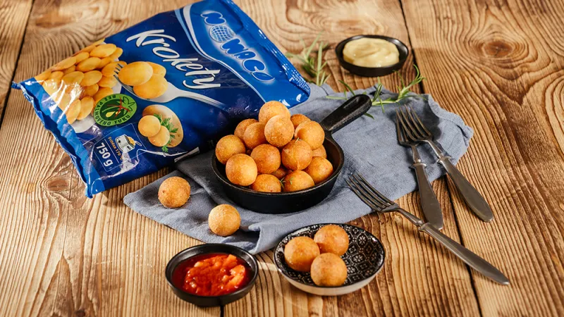 Mrazem zmražené bramborové krokety s omáčkami na dřevěném stole.