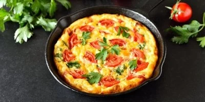 Hotová rajčatová fritáta v železném pánvi s petrželkou.