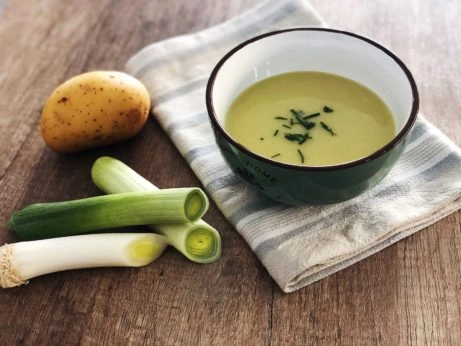 Kremová pórková polévka s bramborami v misce vedle surových ingrediencí.