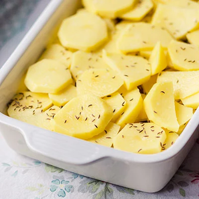 Surové nakrájené brambory s osivo v pekáči před zapékáním.