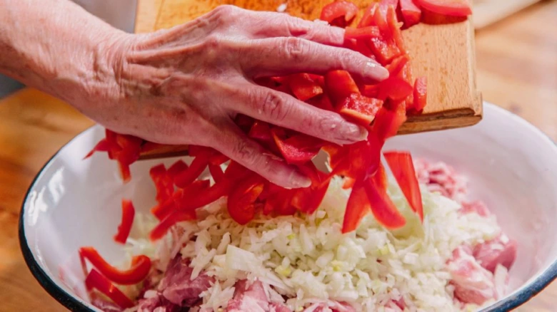 Rozkrojené červené papriky se přidávají do mísy s masem pro guláš.