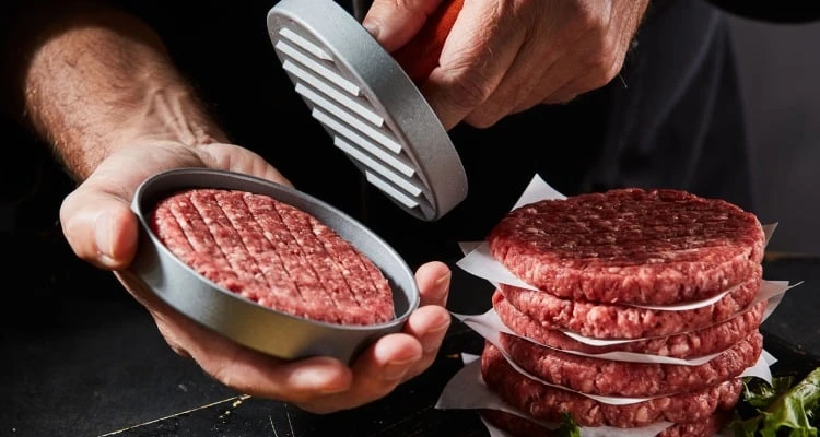 Muž tvaruje syrové hovězí maso na domácí hamburgery pomocí lisu.