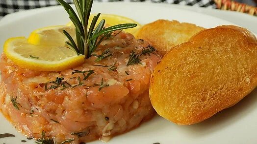 Gravlax losos s citronem, rozmarýnem a chlebíčky na talíři.