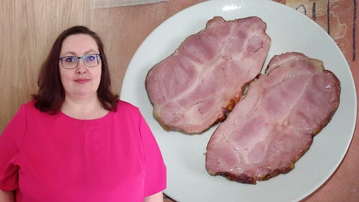 Žena v růžovém tričku stojí vedle talíře s dvěma plátky uzeného masa.