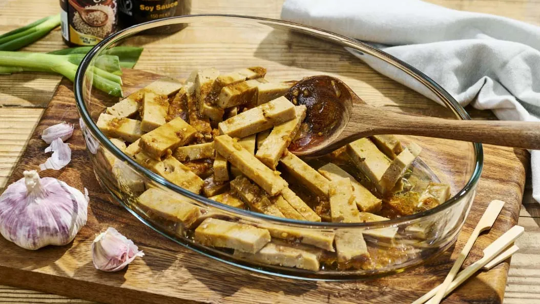 Marinovaný tofu v skleněné mísce s česnekem na dřevěném prknu.