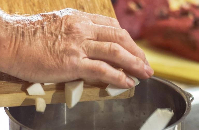Ruka překládá nakrájenou cibuli do hrnce pro recept.