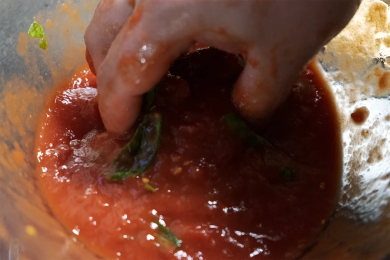 Ruka míchá rajčatovou omáčku s bazalkou pro neapolskou pizzu.