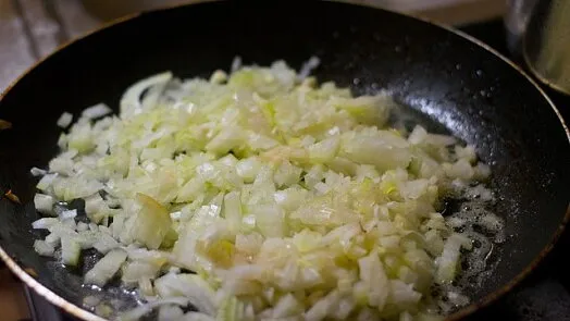 Smažené nakrájené cibule v pánvi pro recept na cuketu.