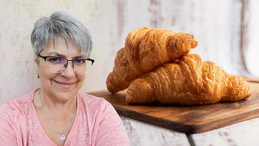 Žena se usmívá vedle dřevěného prkna s třemi domácími croissanty.