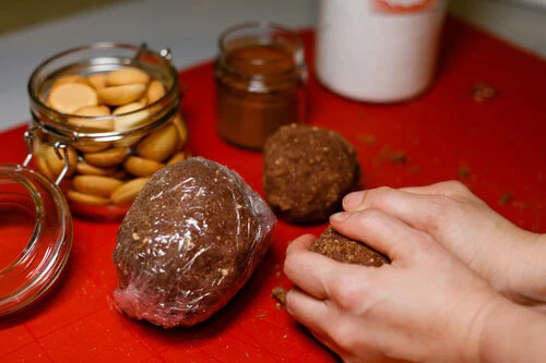 Ruční tvarování kouliček bezpečeného cukroví s surovinami v okolí.