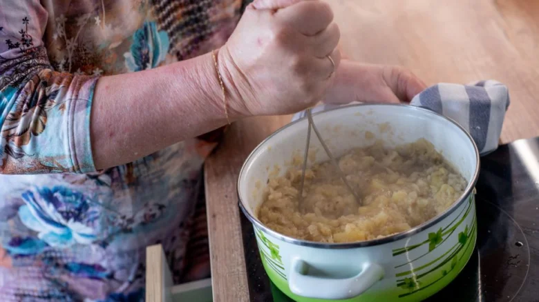 Osoba míchá dušenou kapustu v hrnci na varné desce.