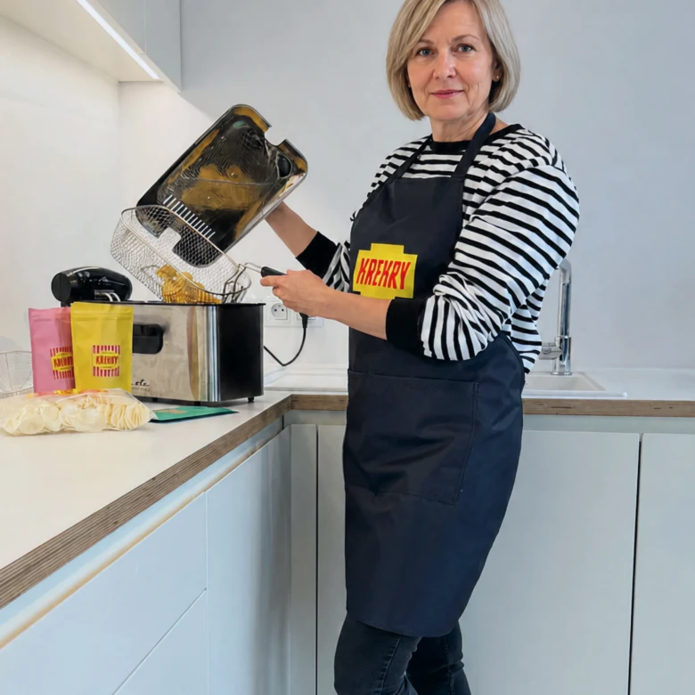Žena smaží bramborové krokety ve fritéze na kuchyňském pultu.