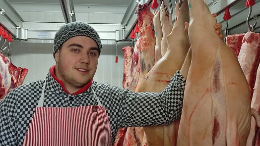 Masný v masném podniku s visícími prasatami.