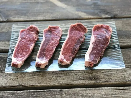 Čtyři kusy syrového masa na skleněném talíři připravené k smažení.