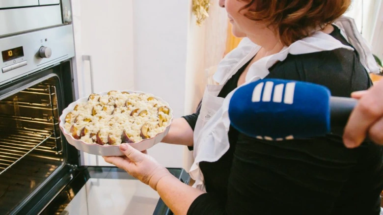 Žena drží švestkový koláč v pekáči u otevřené trouby.