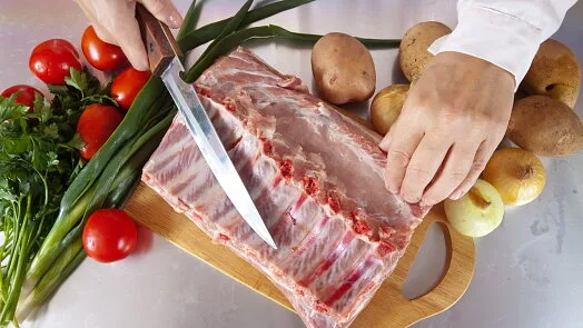 Řezání syrových vepřových žeber s čerstvými zeleninovými ingrediencemi.