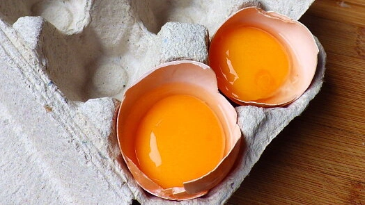 Dva rozbitá vejce s žloutky v kartonovém podložení.
