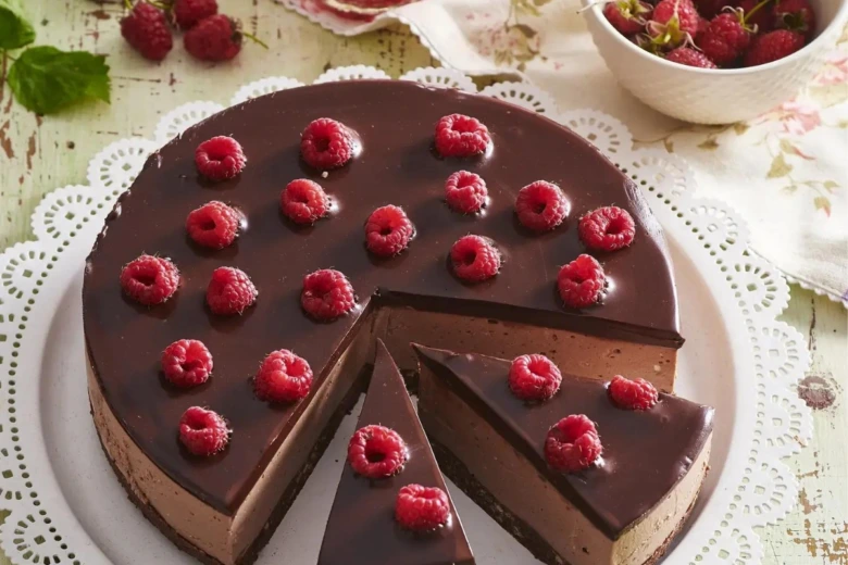 Čokoládový cheesecake s malinami a mascarponem na bílém talíři.