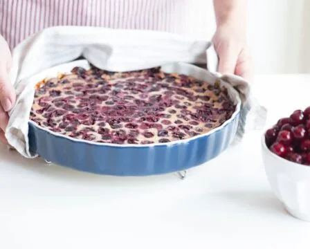 Hot cherry-topped mascarpone cheesecake being taken from the baking dish.