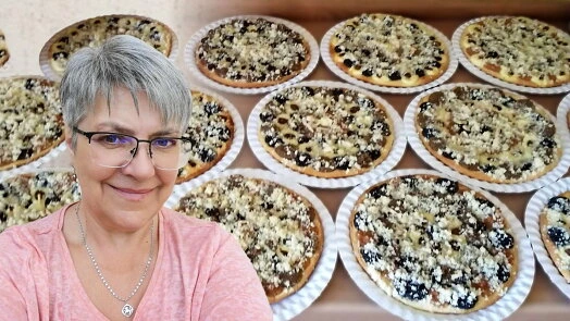 Žena stojí před podnosem s kynutými koláči se švestkami.