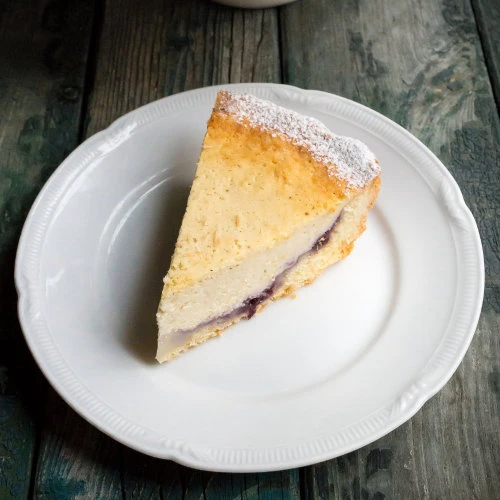 Kousek pečeného tvarohového cheesecaku na bílém talíři.