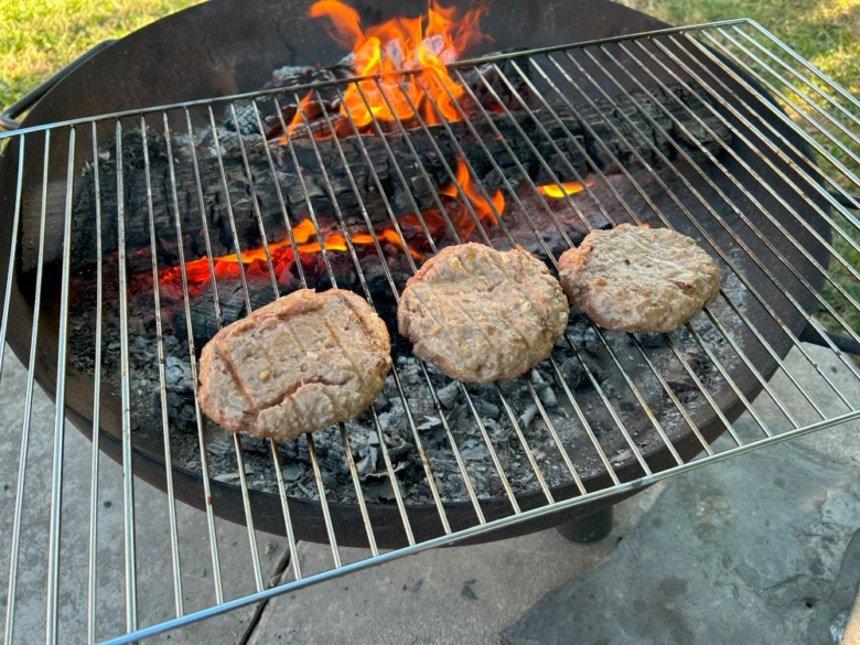 Tři syrové hovězí burgery se grilují nad uhlím.