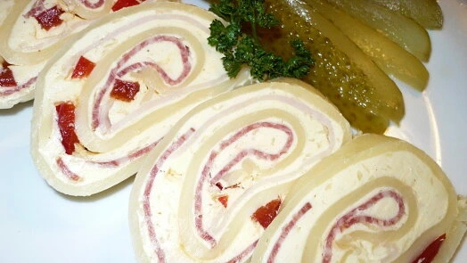 Sýrová roláda s uzeným masem a okurkami na talíři.