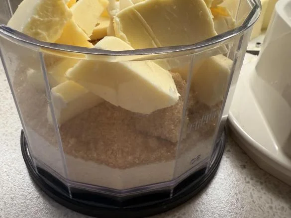 Kusky másla na hnědém cukru v mixéru pro bezpečení cheesecake.