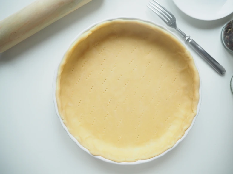 Těsto na quiche v bílém pekáči s prošpikovaným dnem.