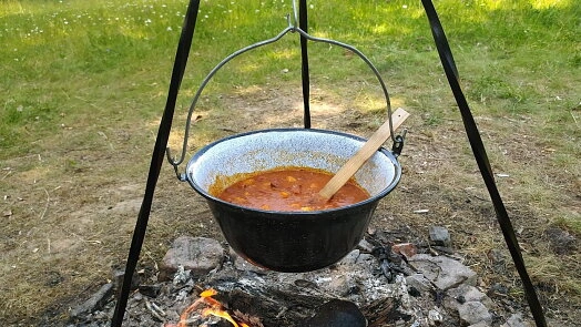Černý hrnec s chilli se vaří na ohni venku.