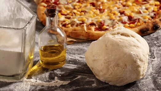 Kus těsta na pizzu s olejem a moukou vedle hotové pizzy.