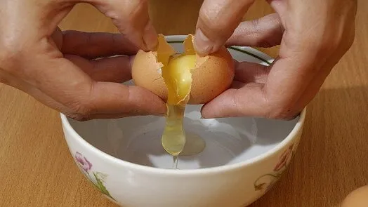 Ruční rozbití vejce do misky pro přípravu těsta.