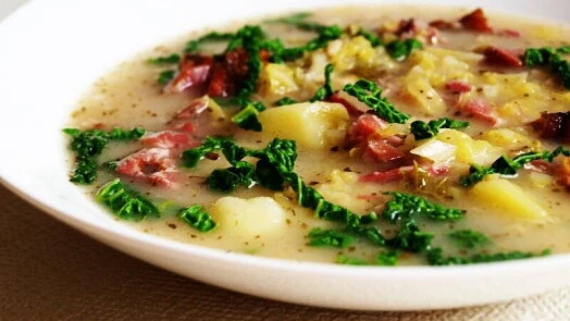Kapustová polévka s masem, bramborami a zeleninou v bílé misce.