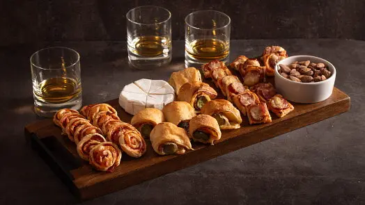 Dřevěná deska s listovým těstem, sýrem Brie a skleničkami whisky.