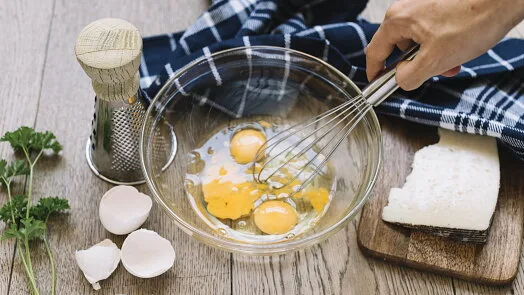 Ruce míchá vejce v misce s ostatními surovinami pro párky.