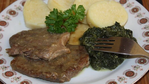 Hotová hovězí roštěná s bramborami a špenátem na talíři.