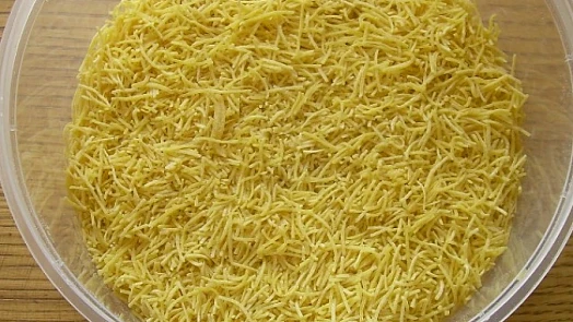 Sušené žloutkové nudle v plastovém míse na dřevěném povrchu.