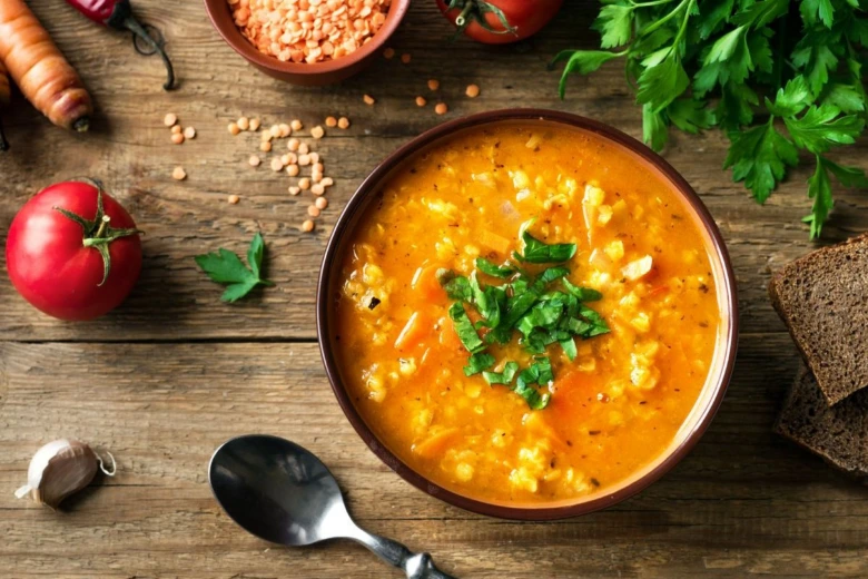 Mísa červené čočkové polévky s petrželkou a surovými ingrediencemi.