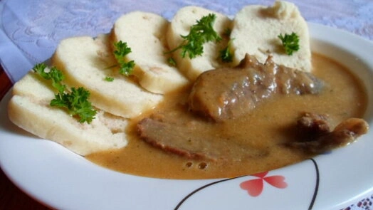 Připravená svíčková s bramborovými knedlíky a omáčkou na talíři.