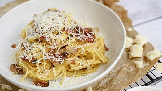 Miska se spagetti carbonarou s nastrouhaným sýrem a křupavými šunkami.
