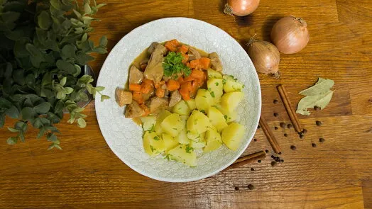 Miska s dušeným vepřovým masem mrkví bramborami na dřevěném stole.